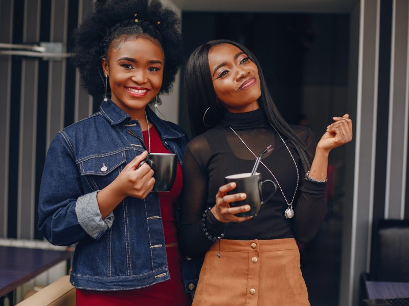 two beautiful and stylish young, dark girls standing in a restaurant and drinking a coffee